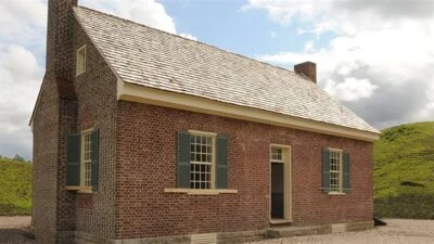 Curator Tour: Ulster Emigration and Black History - Exterior view of Tennessee Rogan Plantation House. Small  red brick house with green window shutters and steep shingled roof